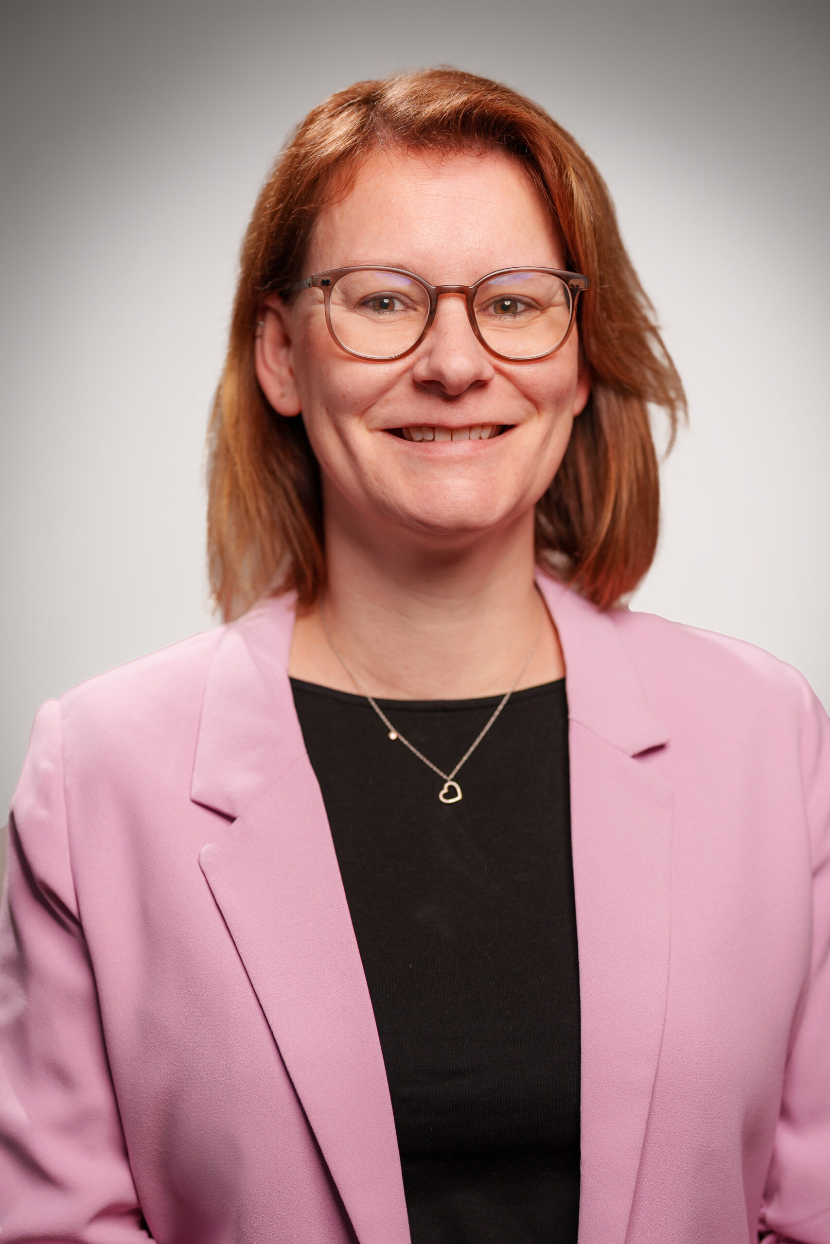 Dies ist ein Portraitbild von Dr. Aukje van Loon. Sie hat schulterlanges hellbraunes Haar und trägt eine farblich passende Brille. Ihr Blazer ist rosa, die Bluse darunter schwarz.